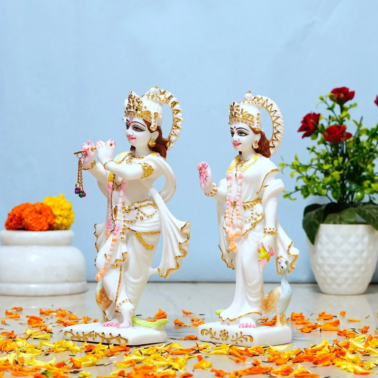 Two statues of deities with floral decorations on a light blue background