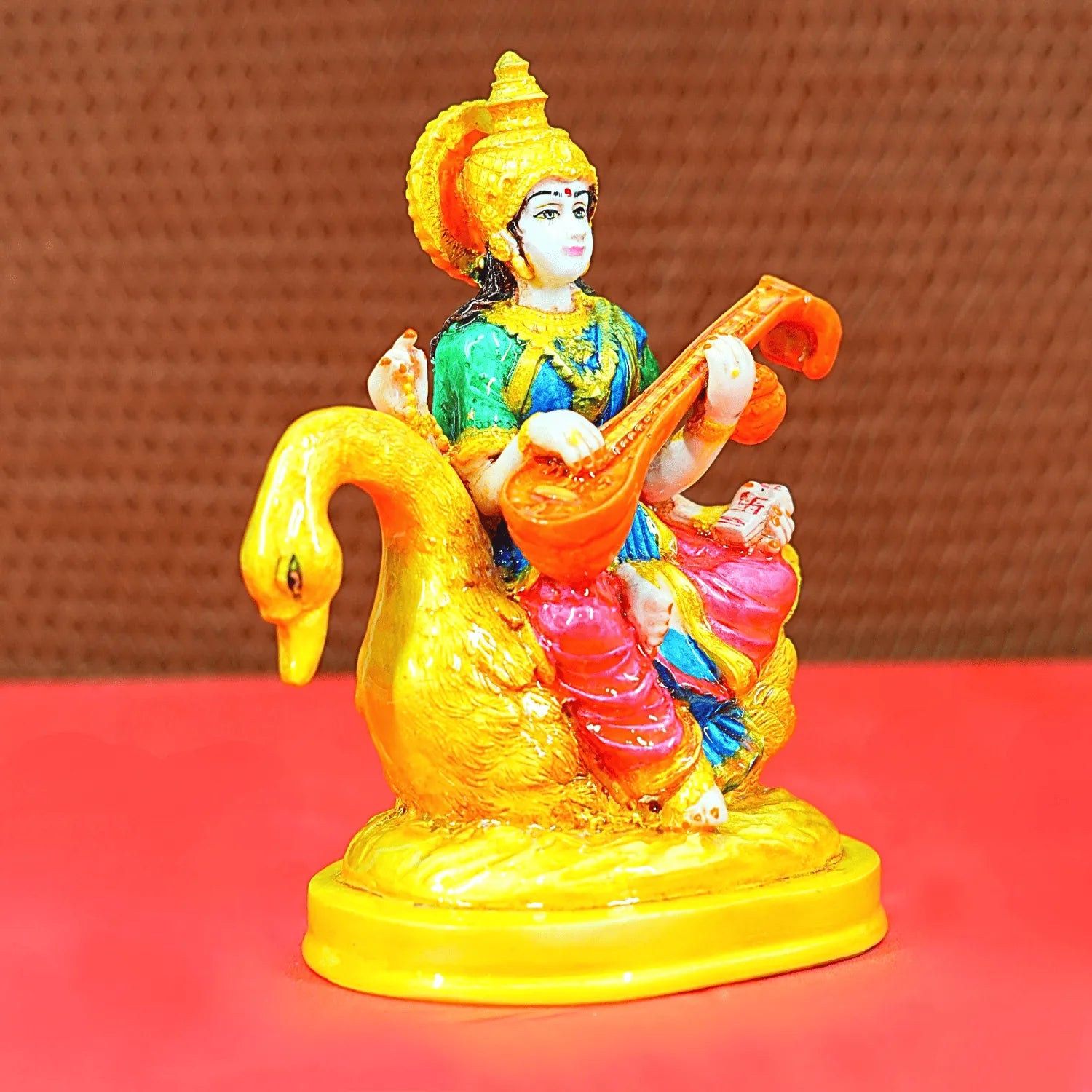 Colorful figurine of a deity playing a instrument on a swan, against a brown background.