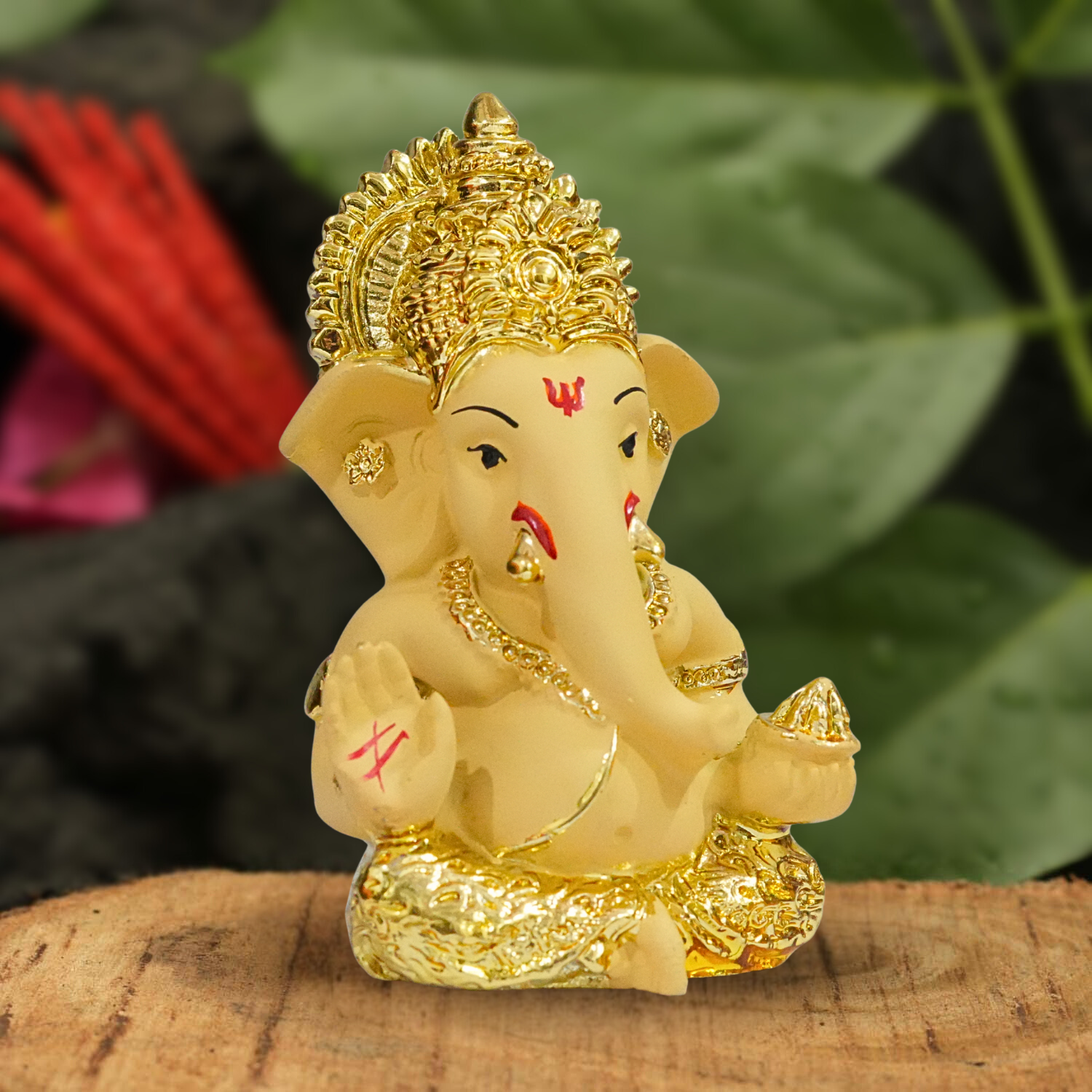 Decorative figure of a deity with gold accents on a wooden surface with green leaves in the background