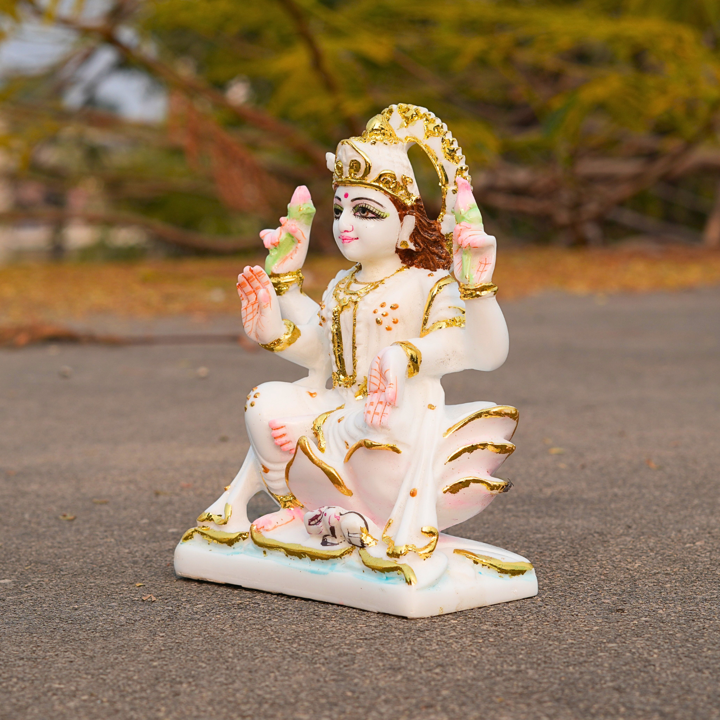Decorative statue of a seated figure with gold and pink details on a blurred natural background