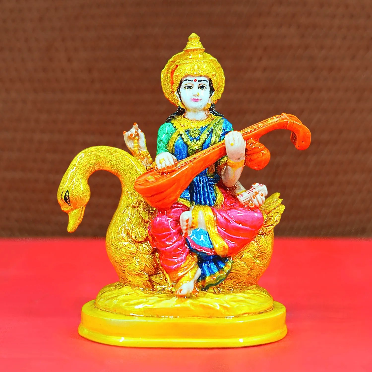 Colorful figurine of a deity playing a instrument on a red platform with a brown background