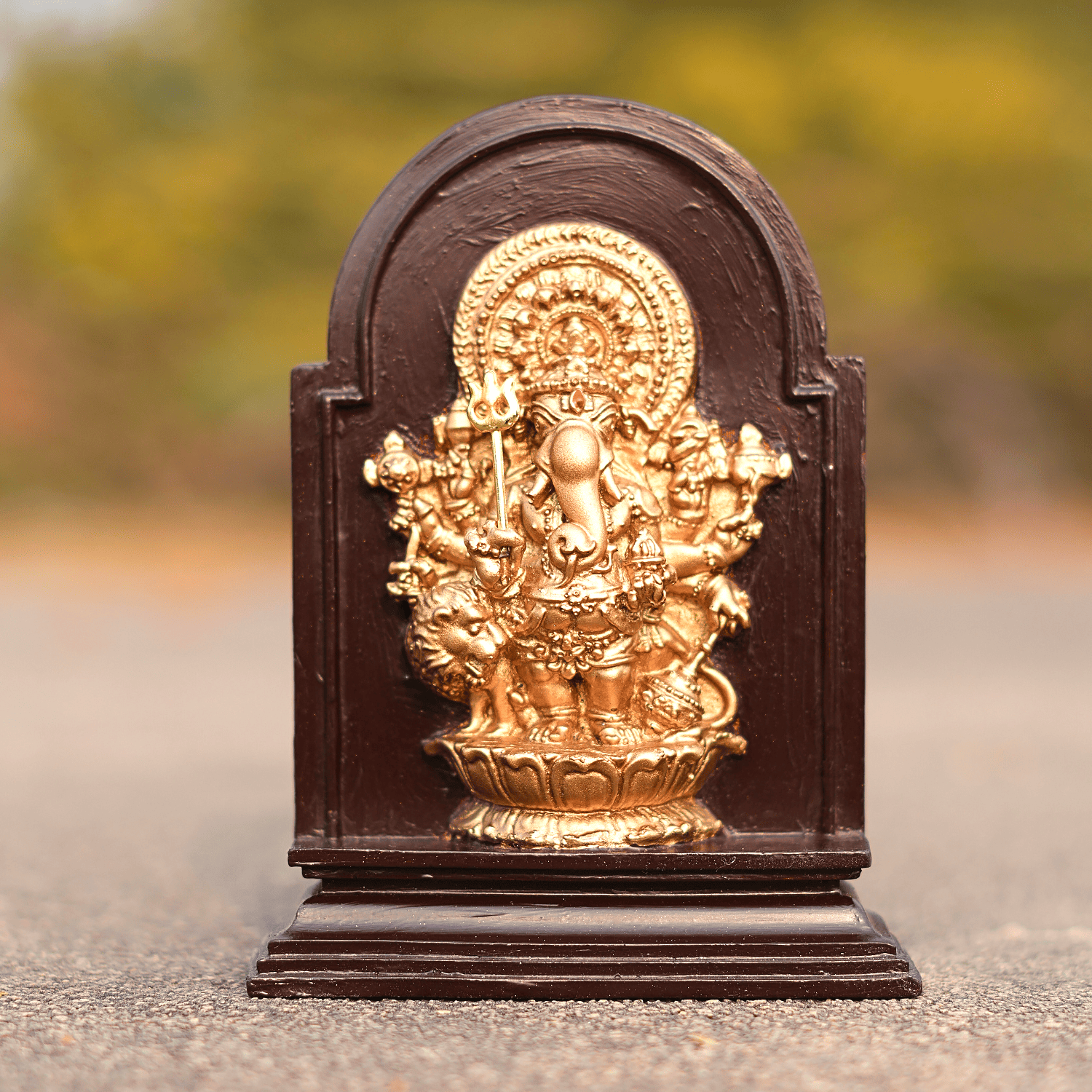 Decorative gold statue on a brown base with a blurred natural background