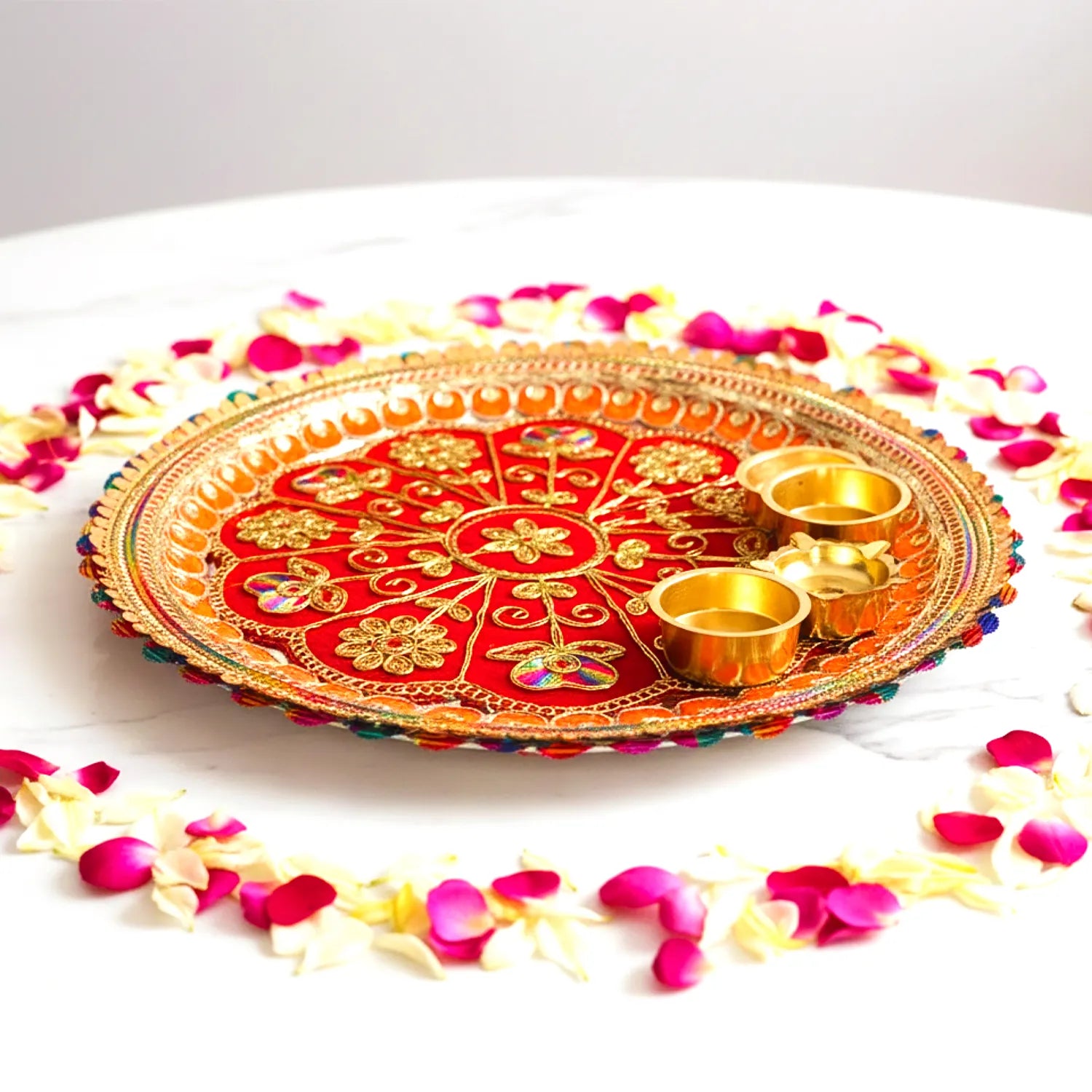 Decorative plate with gold and red design, surrounded by flower petals on a white background